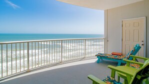 A balcony with a view of the ocean, two green lounge chairs, and a white door.