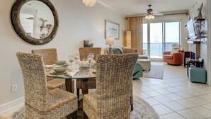 A dining area with wicker chairs and a glass table, a living room with a sofa and armchairs, and a balcony with a view.