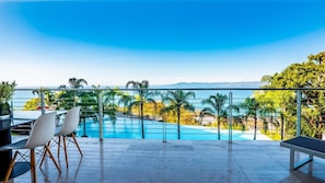 Ein Poolbereich mit freiem Blick auf das Meer, einem Esstisch mit Stühlen und einer Bank.