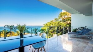 A balcony with a view of the sea, a dining table with chairs, and a lounge area with a chair.