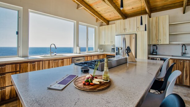 Une cuisine moderne avec des meubles en bois, un grand îlot central et une vue sur l’océan.