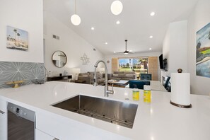 Una cocina moderna con una isla grande, pileta de acero inoxidable e iluminación colgante.