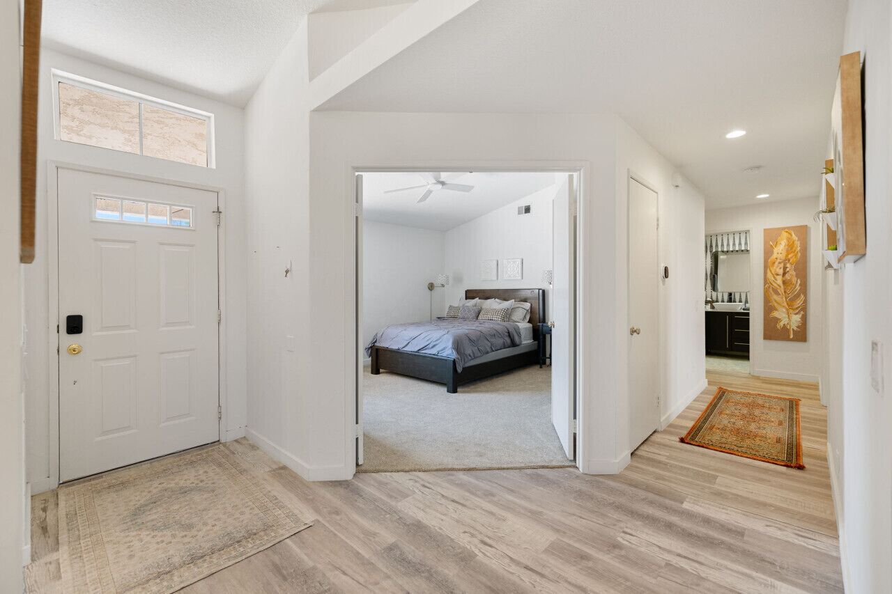 A spacious hallway leading to a bedroom with a bed, a ceiling fan, and a door with a window.