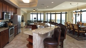 A spacious kitchen with a central island, a dining area with a chandelier, and large windows offering a view. - Best Prices for 4 BR Corner Unit! (Orange Beach)