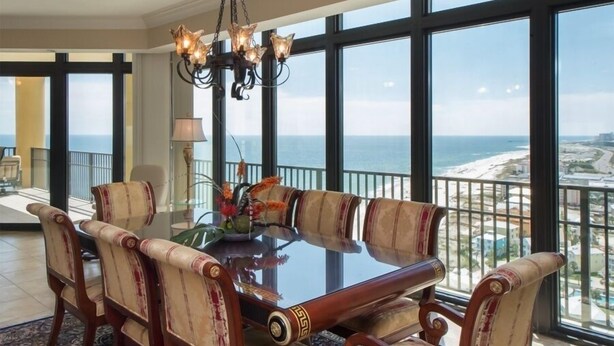 A dining area with a large table, six chairs, and a chandelier. It features large windows with a view of the beach and ocean. - Best Prices for 4 BR Corner Unit! (Orange Beach)