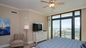 A bedroom with a bed, a TV, a chair, a lamp, and a painting. - Best Prices for 4 BR Corner Unit! (Orange Beach)