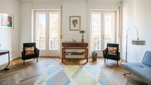 Ein Wohnzimmer mit Fischgrätparkett, zwei Sessel, ein Sofa, ein Couchtisch und eine Stehlampe.