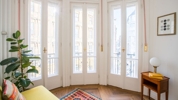 Ein Eckzimmer mit Holzboden, einem gelben Sofa, einem gemusterten Teppich und einer Pflanze.