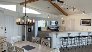 A modern kitchen with a central island, bar stools, and a dining area with wooden chairs. - Beachfront, Plantation, Pet Friendly (Eastpoint)