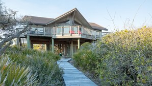 A coastal house with a wooden deck leading to a covered porch and a balcony with red chairs. - Beachfront, Plantation, Pet Friendly (Eastpoint)