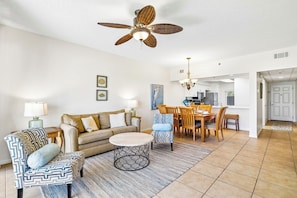 Un soggiorno con ventilatore a soffitto, una poltrona a divano, una poltrona con motivi decorativi, un tavolino rotondo e un'area pranzo con lampadario.