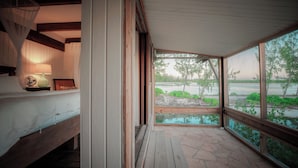 A room with a bed, a bedside lamp, a window with a view of a body of water and greenery. - The Lodge at Parrot Cay, TCI (Caicos Islands)