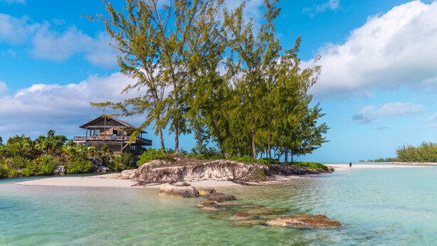 A beachfront property with a wooden structure, clear turquoise waters, and lush greenery. - The Lodge at Parrot Cay, TCI (Caicos Islands)