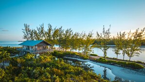 A wooden house with a blue roof and a balcony, surrounded by lush greenery and a calm body of water. - The Lodge at Parrot Cay, TCI (Caicos Islands)