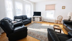 Una sala de estar con un sofá de cuero negro, una mesa de centro de madera y un televisor sobre un mueble.