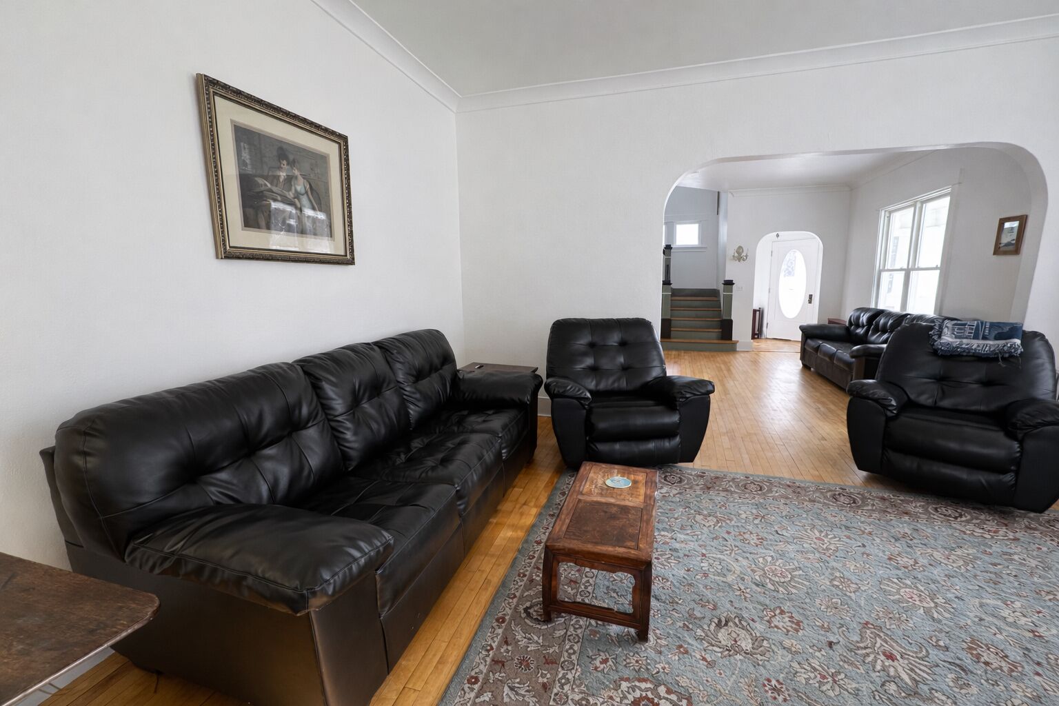 Un salon avec un canapé en cuir noir, deux fauteuils en cuir noir, une petite table basse en bois et un tapis à motifs.