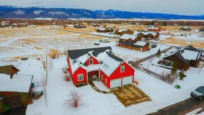 Une maison rouge avec un garage, entourée d’un paysage enneigé et de montagnes lointaines.