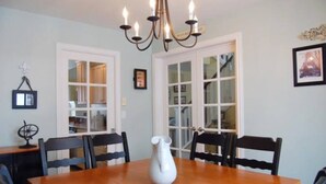 Une salle à manger avec une table en bois, six chaises, un lustre et un vase blanc.
