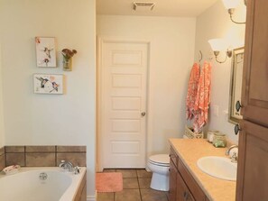 Une salle de bain avec une baignoire, des toilettes, un lavabo et une porte. Des serviettes sont accrochées au mur, et il y a un vase avec des fleurs.