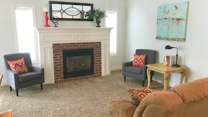 Un salon avec une cheminée, deux fauteuils, un canapé, une petite table et un tableau accroché au mur.
