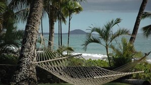 Un hamac est tendu entre deux arbres, au-dessus d’une pelouse, et offre une vue sur l’océan et une île lointaine.