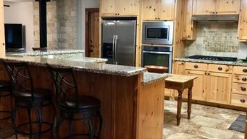 A kitchen with a central island, bar stools, wooden cabinets, a refrigerator, microwave, oven, and a stove.