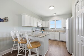 A kitchen with white cabinets, a central island with bar stools, a window, and a refrigerator.