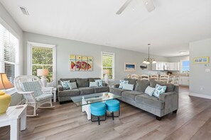 A spacious living room with a sectional sofa, a glass coffee table, and a dining area with white cabinets and a kitchen island.