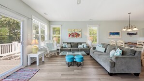 Un vaste espace de vie comprenant un canapé gris, des poufs bleus et une table à manger.