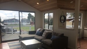 Una sala de estar con sofá, mesa de centro y vistas a una cerca blanca y casas a través de amplios ventanales.