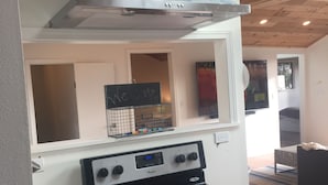 Una cocina con estufa de acero inoxidable, campana extractora y ventana sobre la estufa.