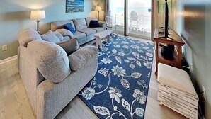 Un soggiorno con divano, tavolino, mobile TV e un'ampia finestra vista spiaggia.