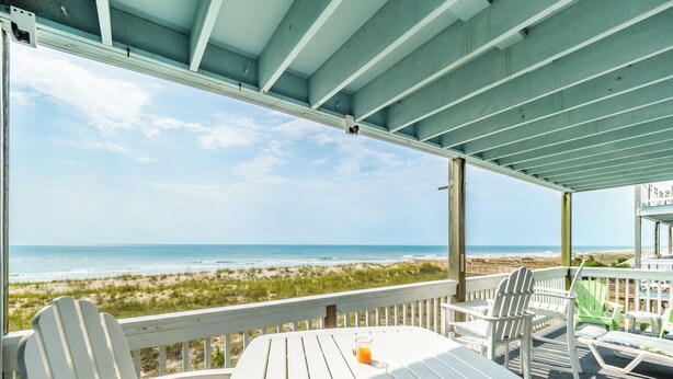 Un'area salotto esterna riparata, con poltrone Adirondack bianche e un tavolo, con vista sulla spiaggia.