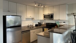 A modern kitchen with white cabinets, stainless steel appliances, granite countertops, and under-cabinet lighting. - Read our Reviews! Newly Updated Condo! Perfect Getaway Steps to Beach & Dining! (Kihei)