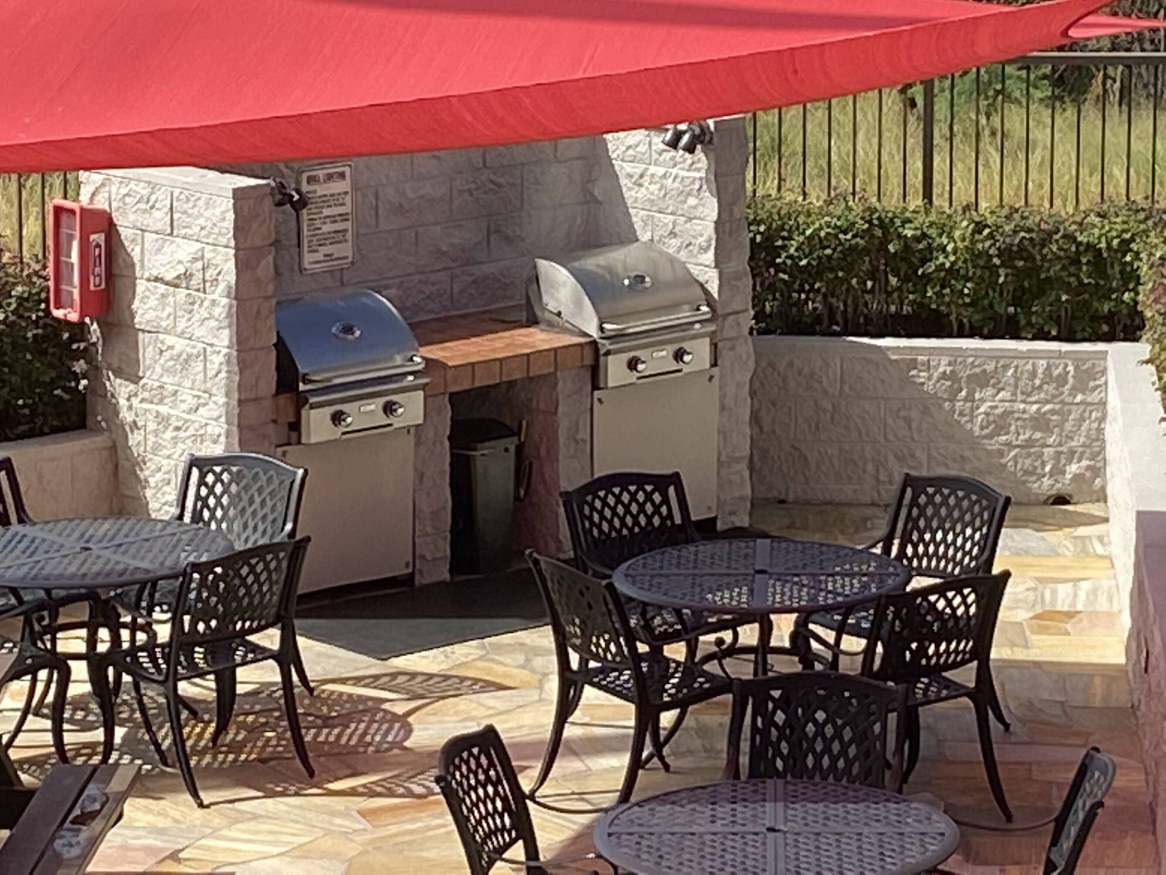 An outdoor patio with a stone wall, a grill, and outdoor furniture.