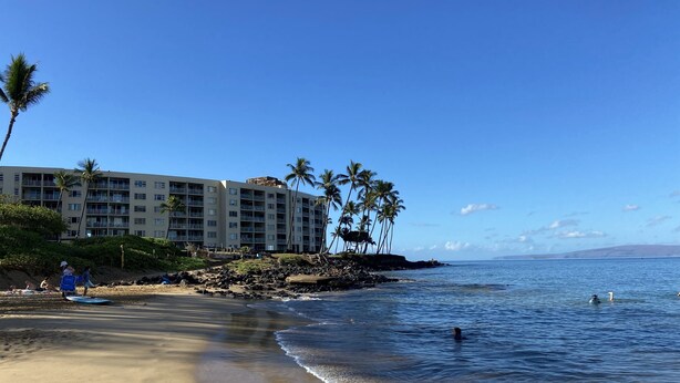 A beachfront hotel with multiple balconies, palm trees, and a clear view of the ocean. - Read our Reviews! Newly Updated Condo! Perfect Getaway Steps to Beach & Dining! (Kihei)