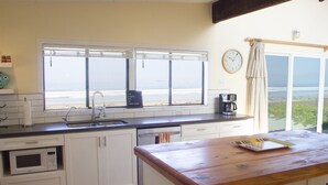 Eine Küche mit einem großen Fenster mit Blick auf den Strand, einer Holzinsel und einer Uhr an der Wand.