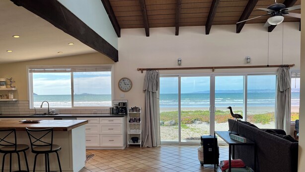 Eine geräumige Küche mit einer großen Kochinsel, eine Essecke mit Barhocker und Blick auf den Strand durch große Schiebetüren.
