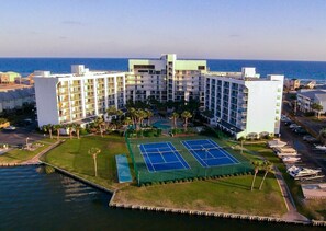 A hotel with multiple floors, a tennis court, and a view of the ocean.