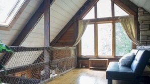 A cozy attic room with a wooden ceiling, a large window with curtains, a cushioned bench, and a wooden floor. - Lake MacBride Cabin & State Park! Near Amana Colonies, Iowa City & Cedar Rapids (Solon)