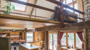 A spacious loft-style living area with a high ceiling, wooden beams, a kitchen with a central island, and a cozy seating area with a sofa and chairs. - Lake MacBride Cabin & State Park! Near Amana Colonies, Iowa City & Cedar Rapids (Solon)