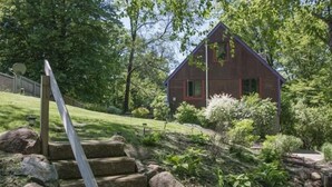 A rustic house with a red exterior, surrounded by lush greenery and a stone staircase leading up to the entrance. - Lake MacBride Cabin & State Park! Near Amana Colonies, Iowa City & Cedar Rapids (Solon)