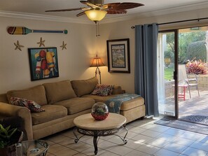A living room with a sofa, a coffee table, a ceiling fan, and a view of the outdoors.