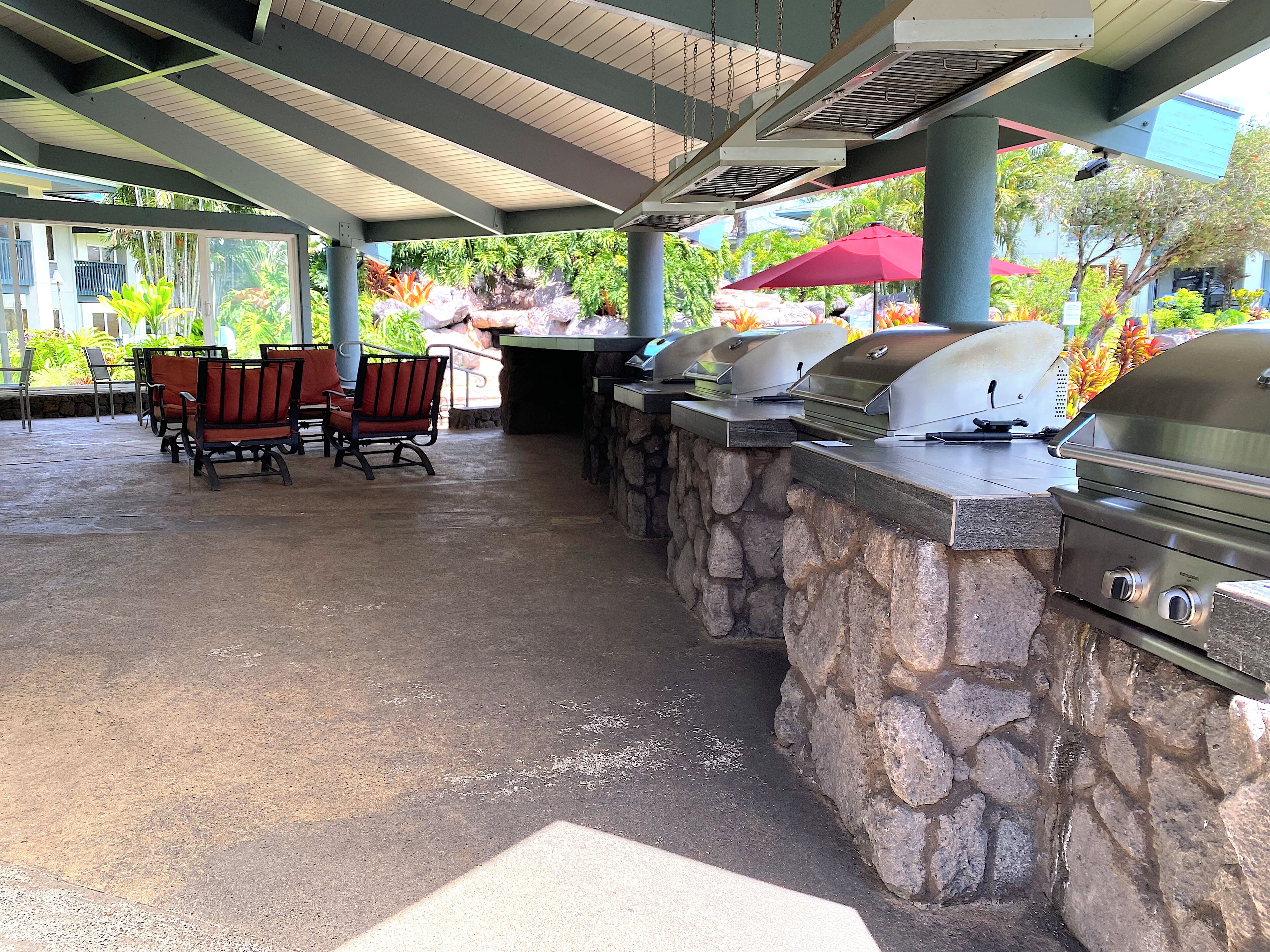 An outdoor patio with stone seating, a grill station, and a covered area with a view of tropical plants.