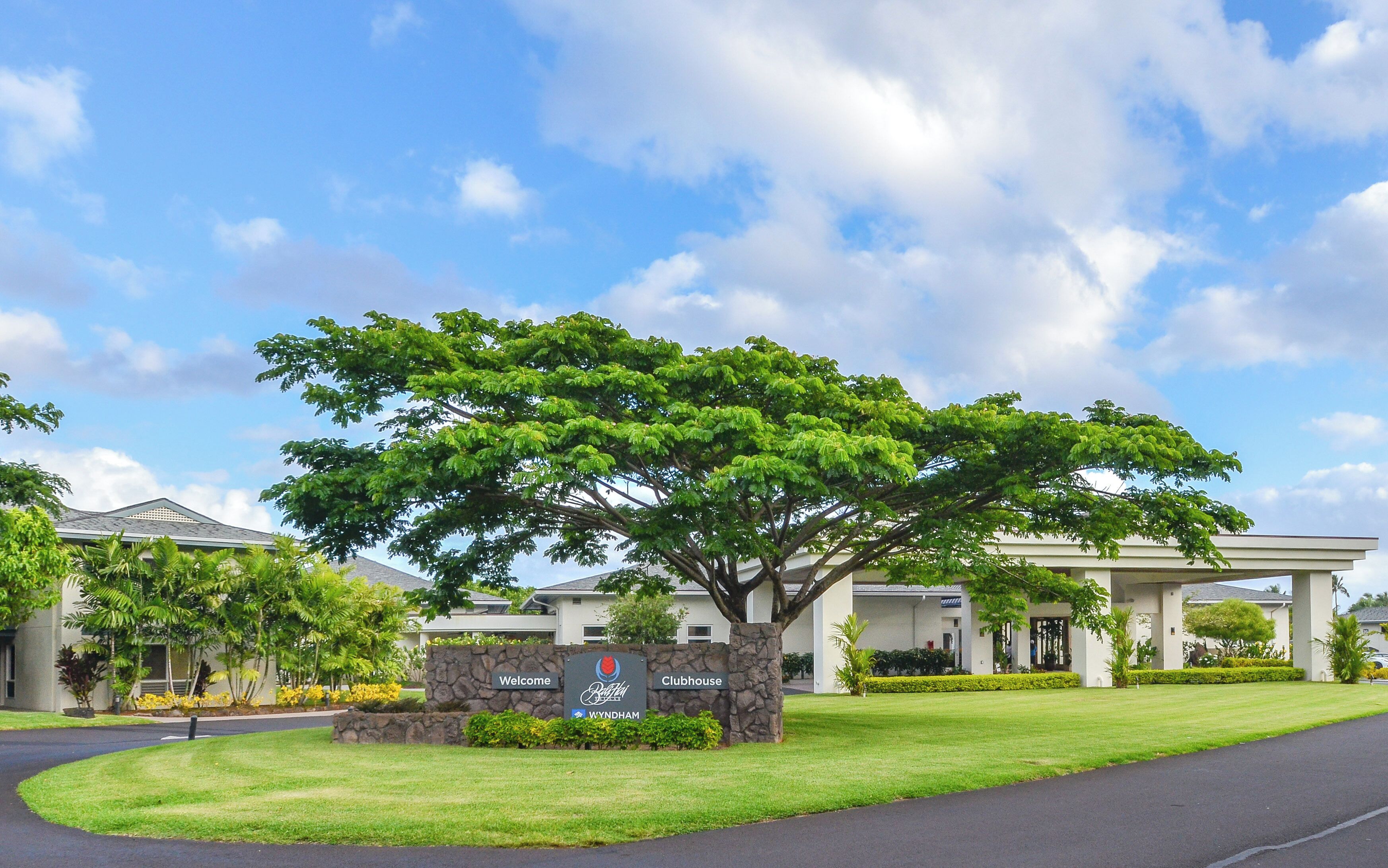 A welcoming sign for a clubhouse with a large tree in front.