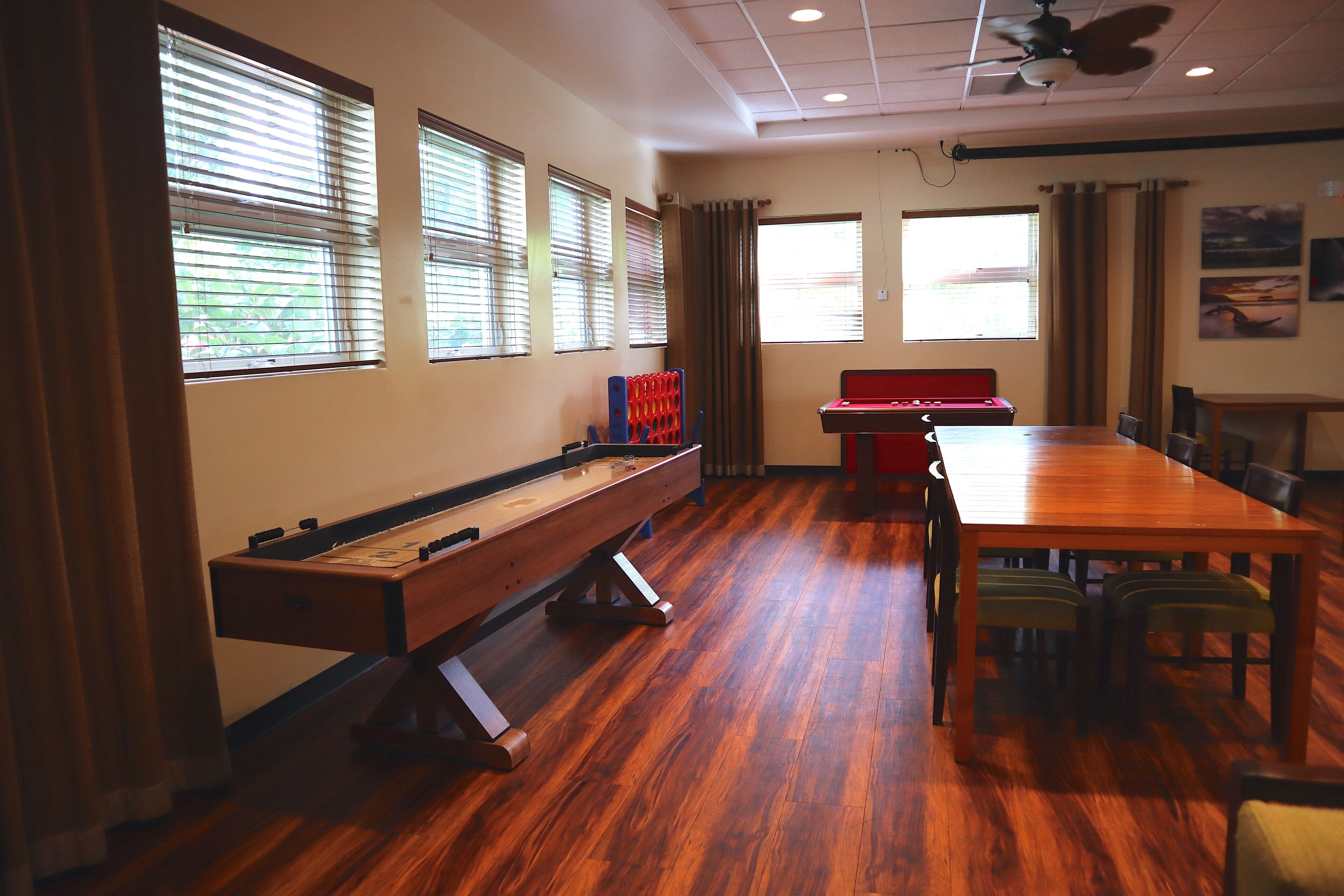 A room with a wooden floor, a pool table, a foosball table, and a long table with chairs.
