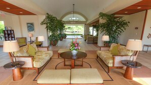 A spacious lobby with a central round table, two sofas, and a bench. There are potted plants and lamps around the seating area. - North Shore Beauty!  2B with Kitchen in Resort near Hanalei (Princeville)