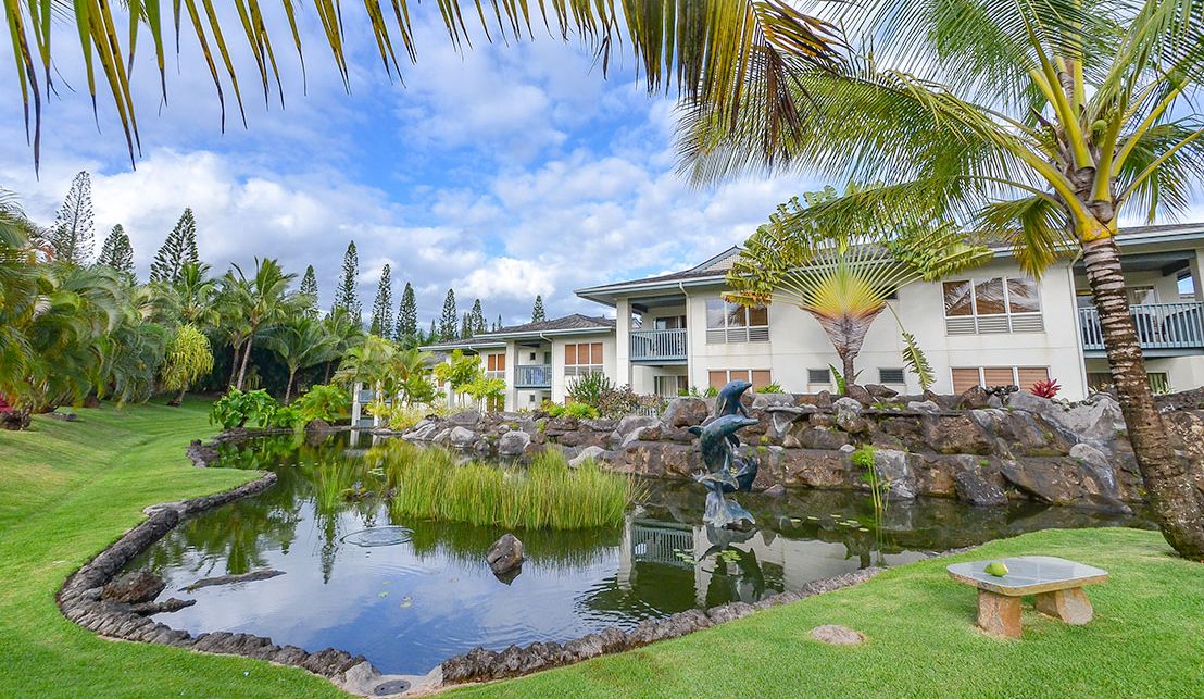 A landscaped garden with a pond, palm trees, and a building with balconies.