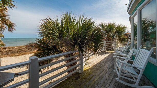 A wooden deck with white rocking chairs overlooking a beach. - A Shore Cure | Panoramic Ocean Views (Kure Beach)