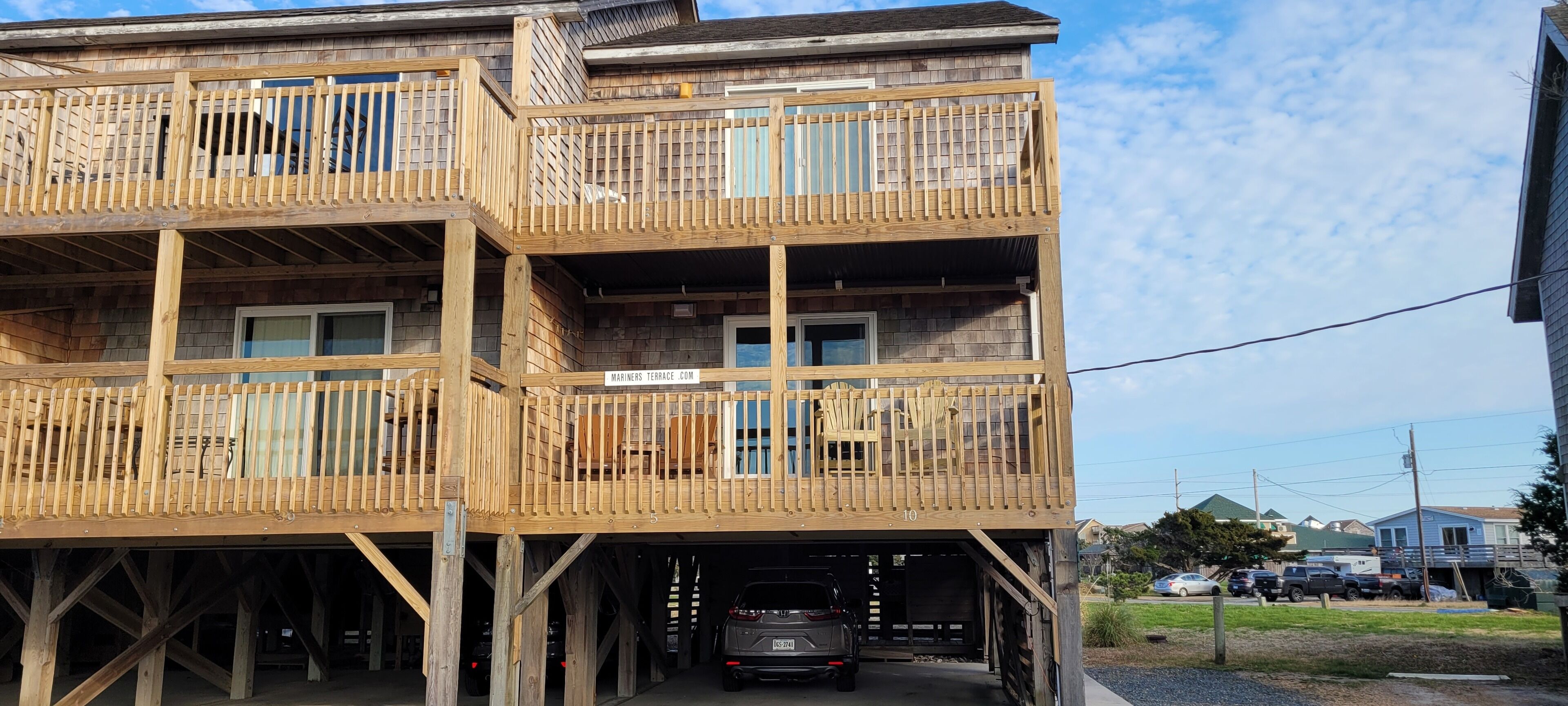 A multi-story wooden building with balconies, a garage entrance, and a visible car parked inside.